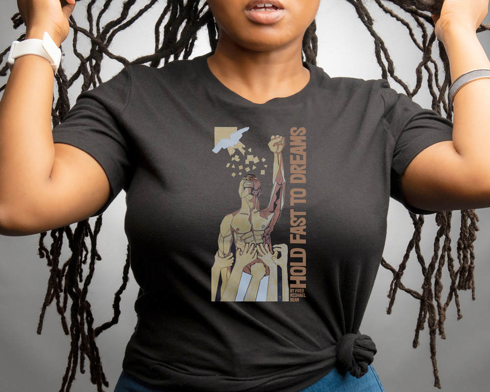 Black woman with dreads wearing black t-shirt. T shirt features a man with his fist upraised. Words "Hold Fast to Dreams' up the side, artist name Fred Michael Beam
