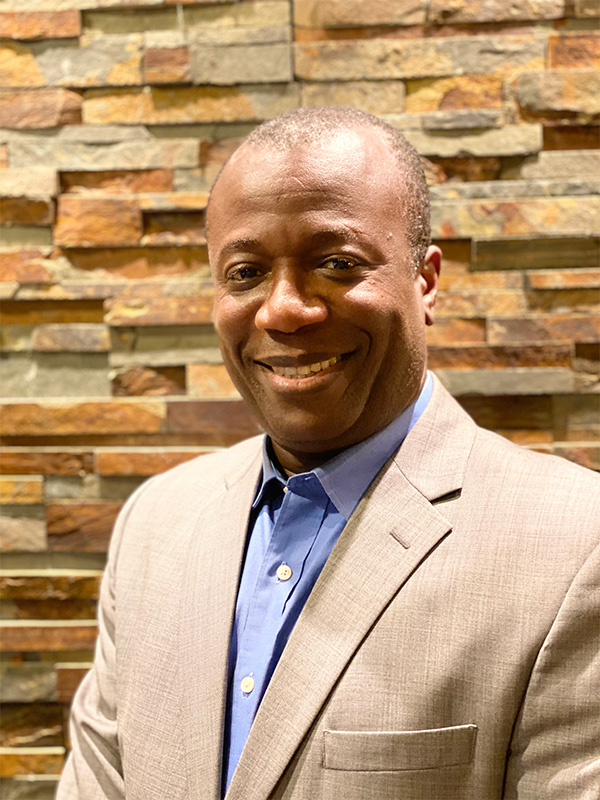 Black man wearing blue shirt and tan suit.