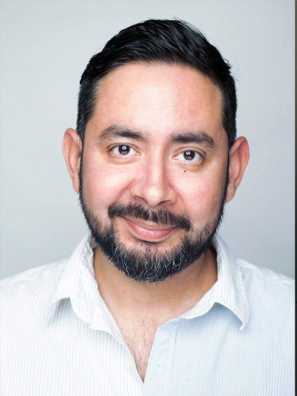 Latinx man with black hair, dark eyes. Wearing white striped shirt.