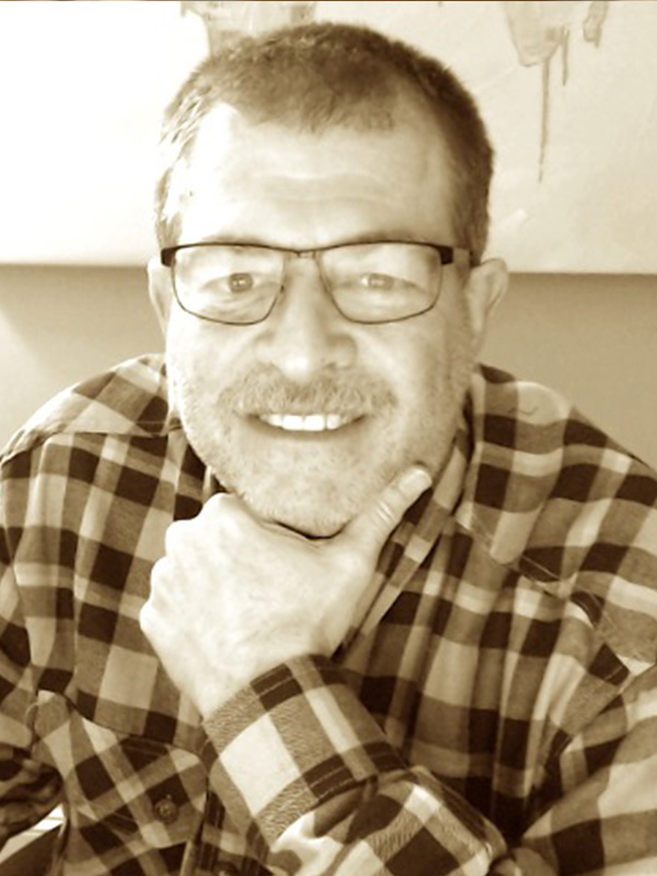 White presenting man with dark hair, glasses, and beard, wearing a plaid shirt. Picture is sepia.