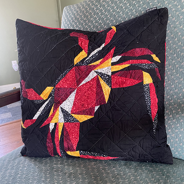 Black pillow, quilted. Red, white, yellow, and black crab pattern.